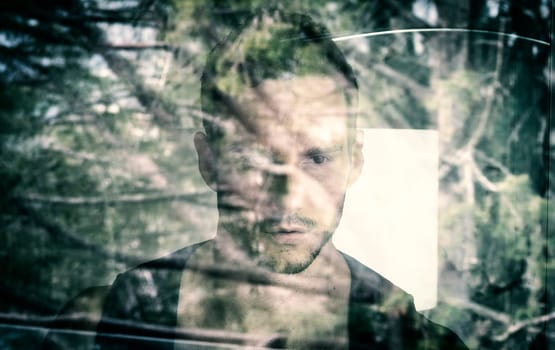 A man looking out of a window with trees in the background