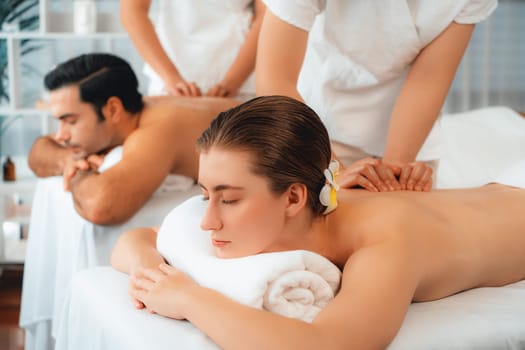 Caucasian couple customer enjoying relaxing anti-stress spa massage and pampering with beauty skin recreation leisure in day light ambient salon spa at luxury resort or hotel. Quiescent
