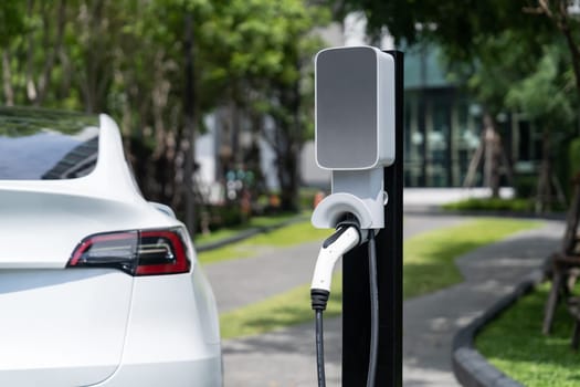 EV electric car charging in green sustainable city outdoor garden in summer. Urban sustainability lifestyle by green clean rechargeable energy of electric BEV vehicle innards