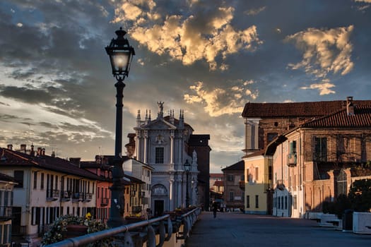 A street light sitting next to a tall building. Photo of a street light illuminating a towering building in the charming town of Bra, Italy