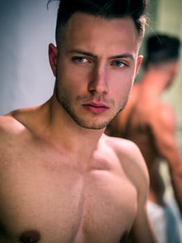 A shirtless man standing in front of a mirror