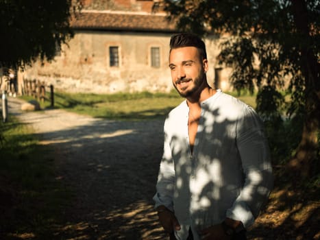 A man standing in front of an old building or farm in the countryside, looking to a side smiling