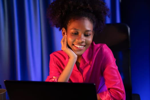 African woman blogger wearing pink shirt with happy face, looking on screen laptop with valued achievement project or get scholarship. Concept of cheerful expression work from home. Tastemaker.