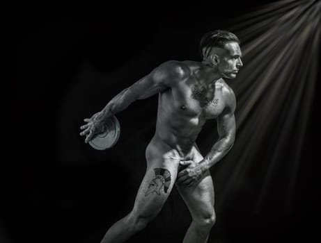 A man totally naked is holding a weight in his right hand, on black