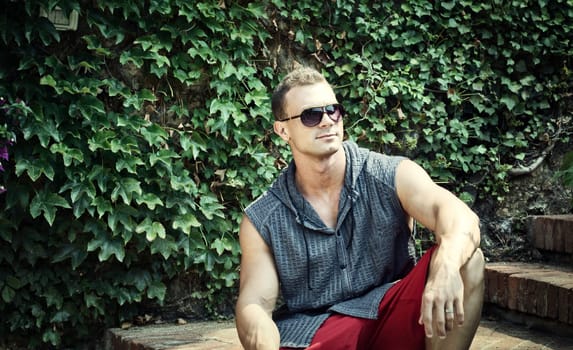 A man wearing sunglasses sitting on a stone step. Photo of a stylish and confident young man sitting on a stone step wearing sunglasses