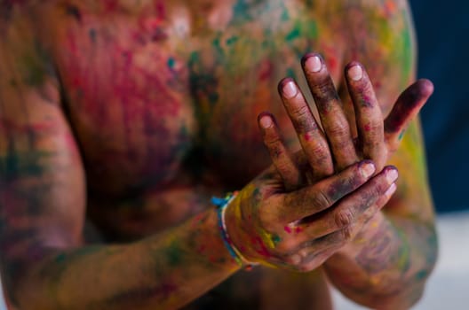 A person covered in paint holding their hands together. Photo of a person covered in colorful paint with hands clasped together