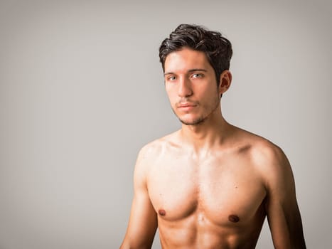 A man without a shirt posing for a picture in studio. Photo of a young and handsome shirtless man posing with captivating green eyes