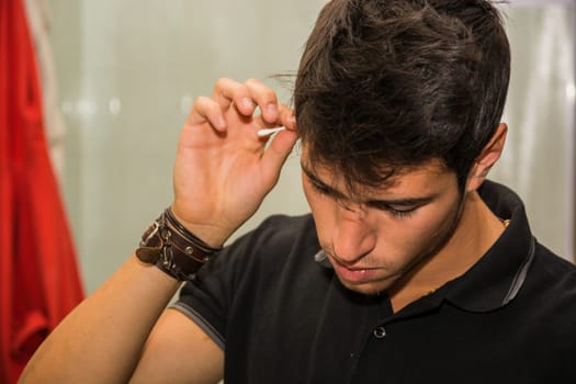 A young handsome man is cleaning his ears with a cotton stick. Photo of a man cleaning his ears with a cotton stick