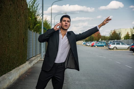 A man in a suit talking on a cell phone, hailing a taxi with his hand raised, calling a cab