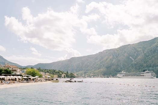 Huge cruise ship sails along the Bay of Kotor past the coast with mountains in the background. High quality photo
