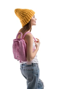 Pretty happy teenager in knitted yellow hat, white t-shirt and torn jeans with pink knitted bag isolated profile shot