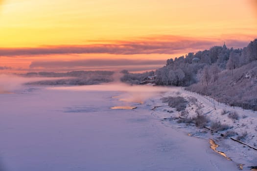 Beautiful Russian winter landscape with frozen river, embankment and street lamps against pink and yellow sunset view