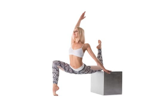 Slim blonde in sportswear sitting in a split on a cube isolated view