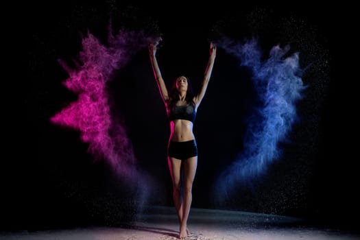 Young woman in black clothes standing with hands up in blue and pink smoke