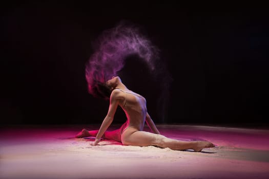 Slim woman sitting in splits and waving with long hair making cloud of white powder in pink light