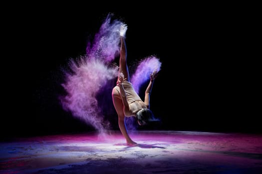 Slim girl wearing beige body dancing in color dust in dark room