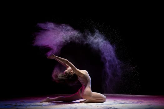 Gorgeous woman wearing beige body sitting in a split in color dust in dark room profile shot
