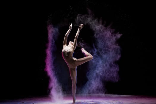 Graceful slim woman dancing expressively in colored flying dust on black background