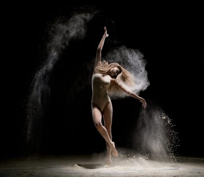 Gorgeous girl wearing beige body dancing in white dust in dark room