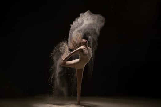 Woman wearing beige body dancing gracefully in white dust cloud profile shot in the dark room