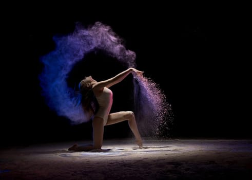 Gorgeous brunette wearing beige body staying on her knees in color dust in dark room profile shot