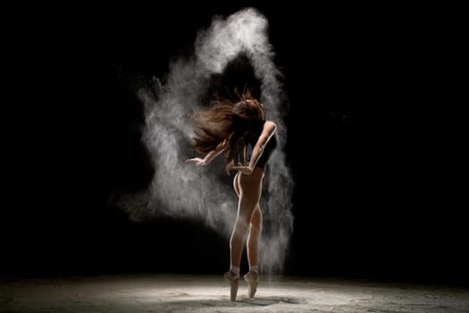 Gorgeous brunette wearing gray body dancing in white dust in dark room rearview