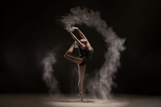 Brunette wearing gray body dancing gracefully in white dust cloud profile shot in the dark room
