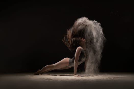 Brunette lying on the floor arching her back in white dust cloud shot in the dark room