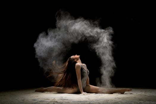 Gorgeous brunette wearing gray body sitting in a split in white dust in dark room profile shot