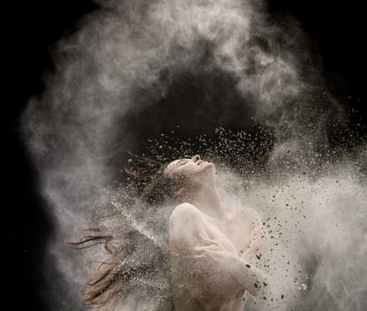 Woman in the nude in white dust cloud in the dark room cropped shot