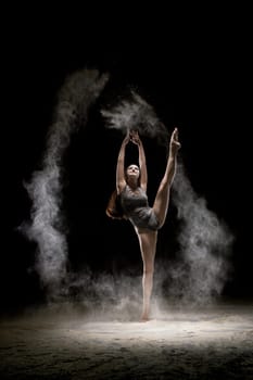 Gorgeous brunette wearing gray body dancing in white dust in dark room