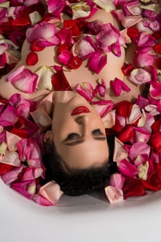 Gorgeous brunette in the nude having bath with pink and red rose petals high angle shot