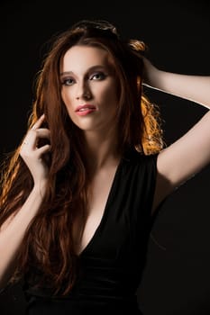 Portrait of beautiful brunette with long hair wearing elegant black dress and posing sensually at camera on black background
