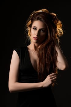 Gorgeous long-haired brunette wearing sexy black dress cropped shot in the dark room