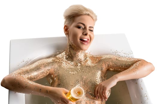 Happy blonde with gold shiny skin in the nude having bath in foam holding a glass of champagne isolated view