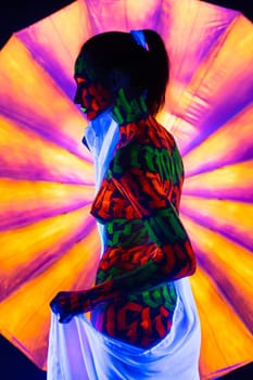 Woman with artistic UV bodyart with white ribbon in her hair and white cloth around her waist full-length reraview against colorful background