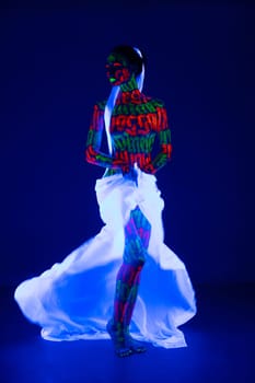 Girl with beautiful artistic UV bodyart with white ribbon in her hair and white cloth around her waist full-length view against dark blue background
