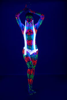 Slim girl with beautiful UV bodyart wearing white pants and white ribbons in her hair full-length shot against dark blue background