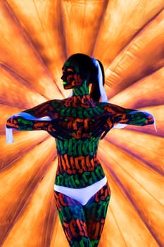Girl in white pants with beautiful UV bodyart cropped view against orange background
