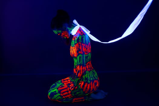Girl with beautiful UV bodyart sitting on the floor white ribbion tied on her neck like a leash profile shot