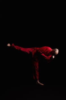 Male wearing red costume doing exercises profile shot in the dark room