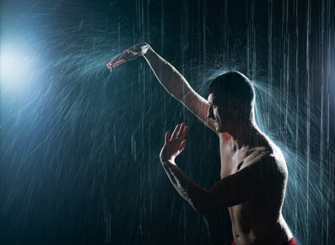 Shirtless man practicing gymnastics under the rain in the dark profile cropped shot