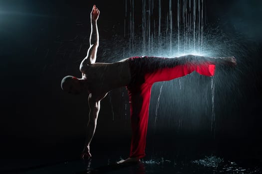 Shirtless man in red trousers practicing qigong under the rain in the dark profile shot