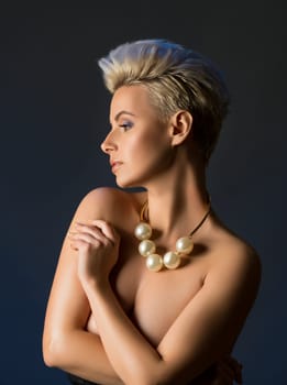 Gorgeous blonde topless with fashionable haircut wearing only beads waist up profile portrait