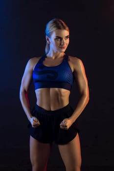 Athletic slim girl wearing top and shorts cropped view against dark wall