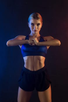 Athletic slim woman wearing top and shorts cropped view against dark wall