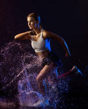 Young girl in sexy sportswear running in the dark in water splashes full-length shot