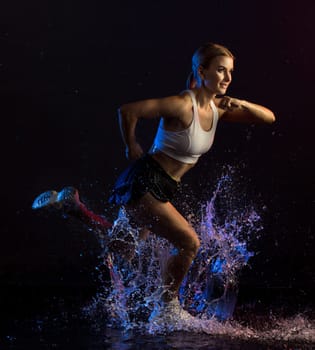 Fitness model in sexy sportswear running in the dark in water splashes full-length shot