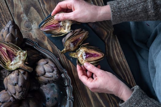 Woman cleaning fresh artichokes and cooking on wooden table, rustic still life top view,concept of healthy eating and fine dining,
