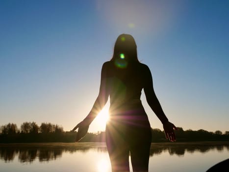 Woman standing on sadhu board, process of standing barefoot on nails, yoga practice and meditation outdoors, autumn day near lake at sunrise
